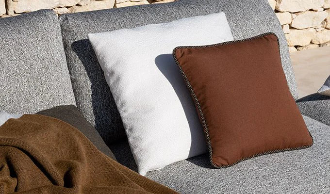 Gray sofa with brown and white cushions against a stone wall background