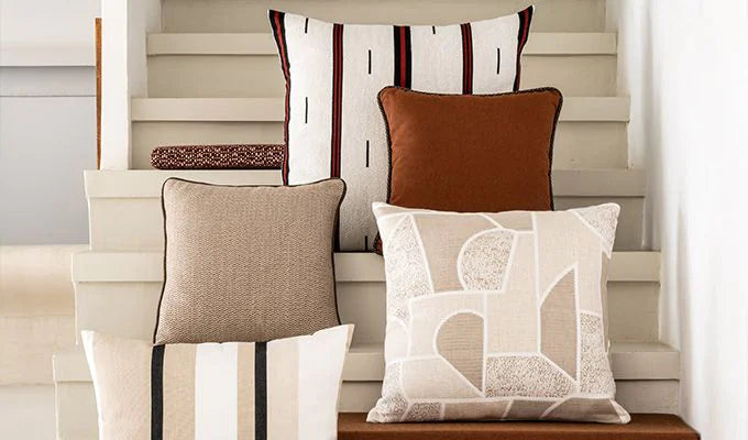Four decorative pillows on a wooden bench with a neutral background