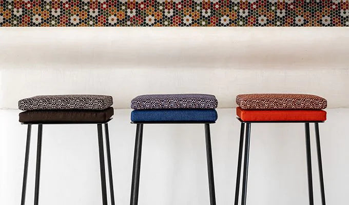 Three bar stools with patterned cushions in gray, blue, and red against a white wall.