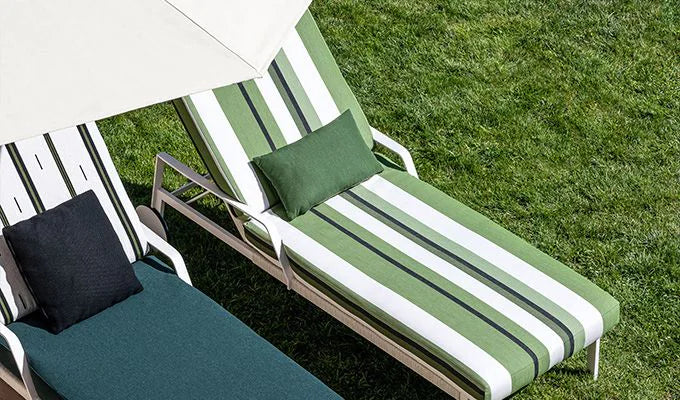 Two lounge chairs with green and white striped cushions on a grassy background