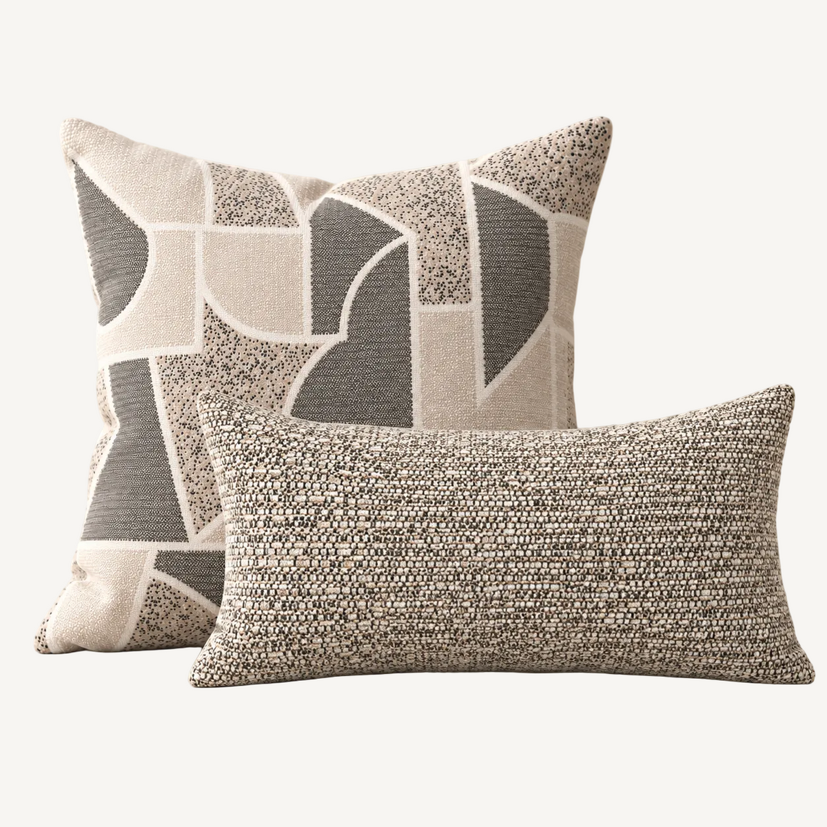 Two decorative throw pillows in a neutral studio setting. The larger square pillow behind features an abstract geometric pattern in gray, beige, and white textured fabric.