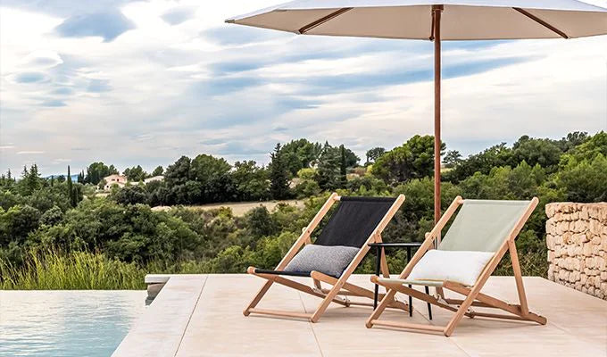 Two lounge chairs under an umbrella with a scenic view of trees and sky.