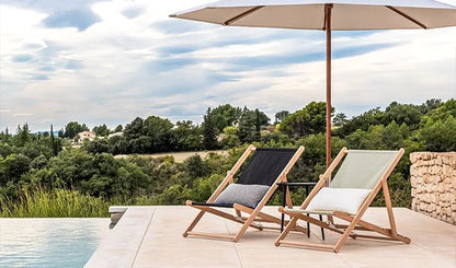 Two lounge chairs under an umbrella with a scenic view of trees and sky.