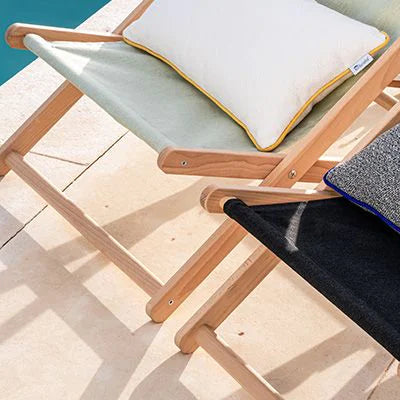 Two lounge chairs with cushions on a wooden deck by a pool.