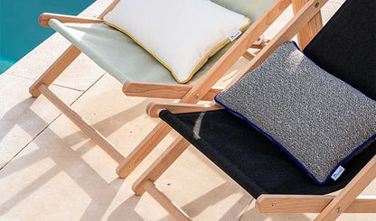 Two lounge chairs with cushions on a wooden deck by a pool.