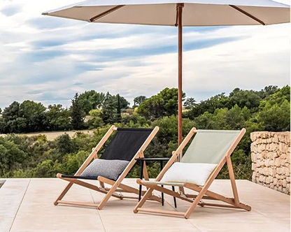 Two lounge chairs under an umbrella with a scenic view of trees and sky.