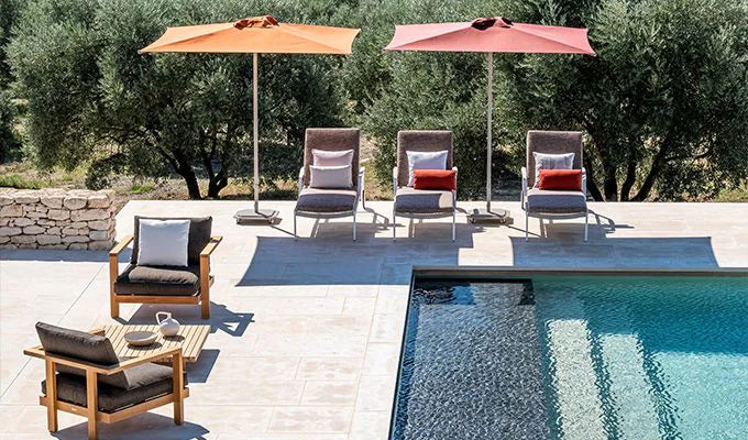 Outdoor patio area with lounge chairs, tables, and umbrellas by a pool.
