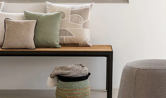 Bench with decorative pillows and a small stool with a blanket in a room setting.