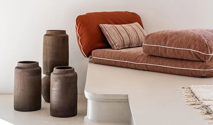 Brown textured vases on a white surface with a brown cushioned chair in the background.