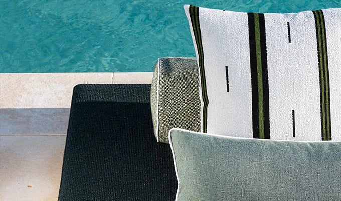 Decorative pillows with striped patterns on a chair by a poolside.