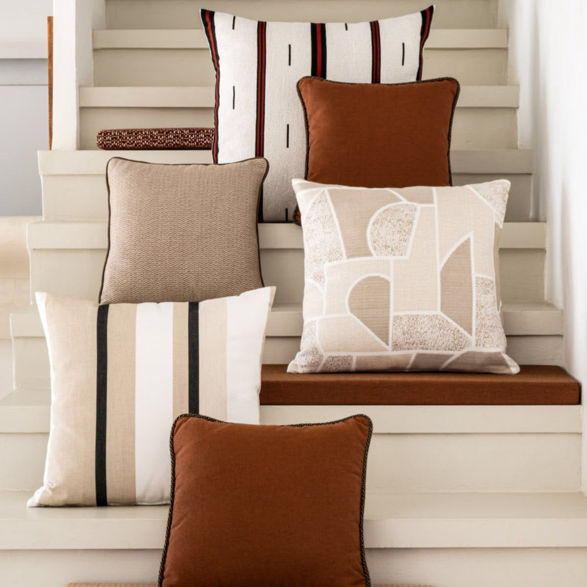 A collection of decorative throw pillows in various colors and patterns, styled on and around neutral-toned wooden stairs.
