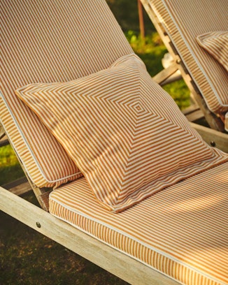 Beige lounge chair with striped cushions on a grassy background
