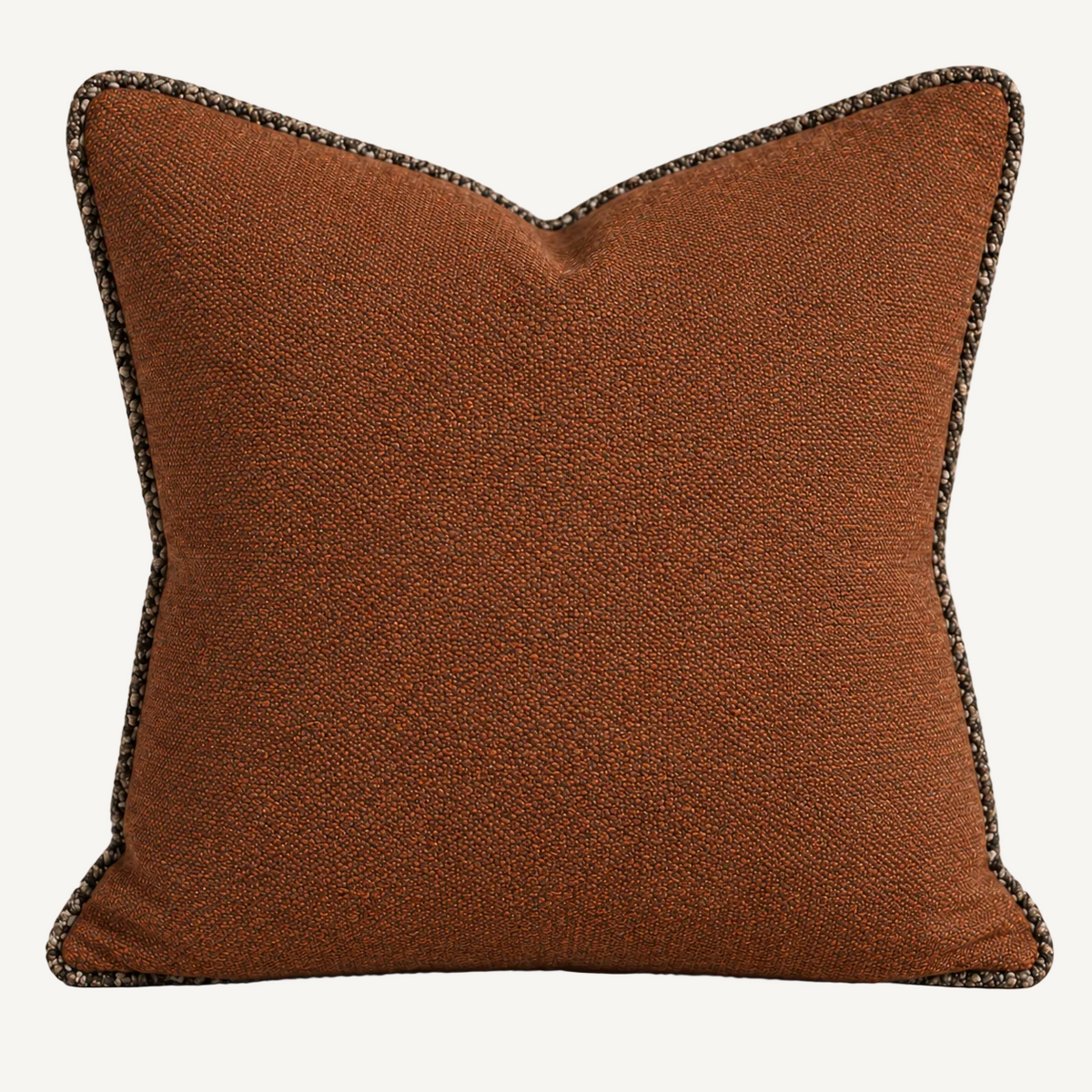 A square decorative throw pillow in a textured rust-brown fabric with a dark gray and beige braided trim, shown against a neutral beige background.