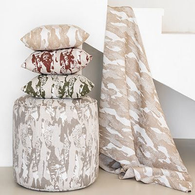 Decorative pillows and blanket on a textured stool against a white wall.