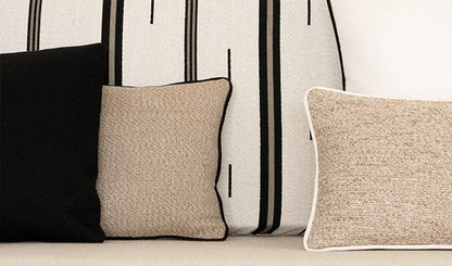 Three pillows in black, beige, and white on a sofa with a striped wall in the background.